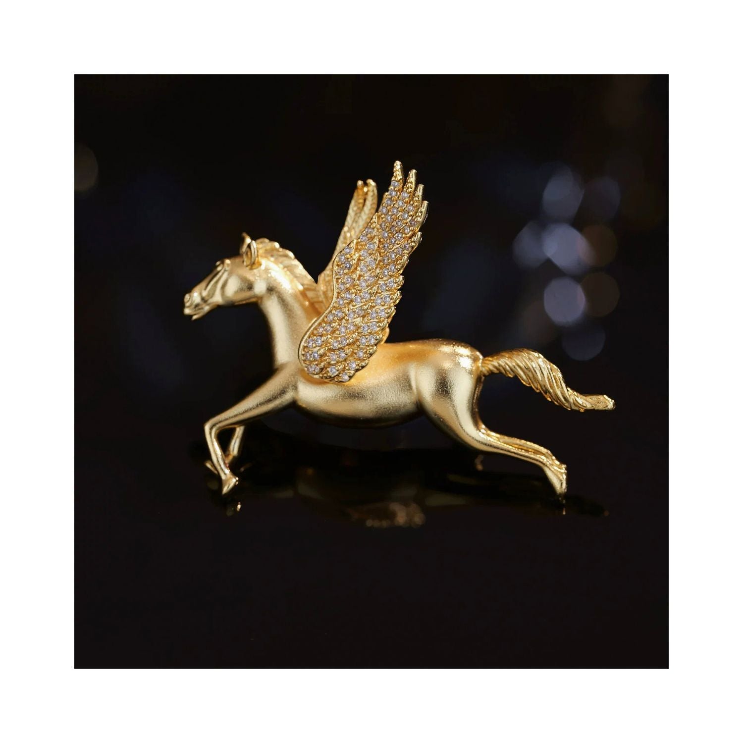 Close-up of Wings of Inspiration Pegasus pavé horse brooch in gold tone on a dark background, highlighting the sculpted flying horse form, crystal-set wing, and polished metallic finish.