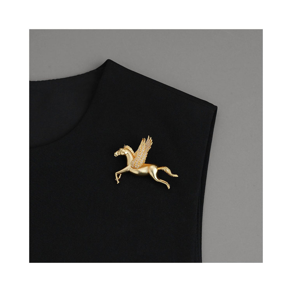 Gold-tone Wings of Inspiration Pegasus pavé horse brooch styled on a black lapel, showing an elegant flying horse silhouette and refined statement styling.