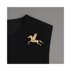 Gold-tone Wings of Inspiration Pegasus pavé horse brooch styled on a black lapel, showing an elegant flying horse silhouette and refined statement styling.