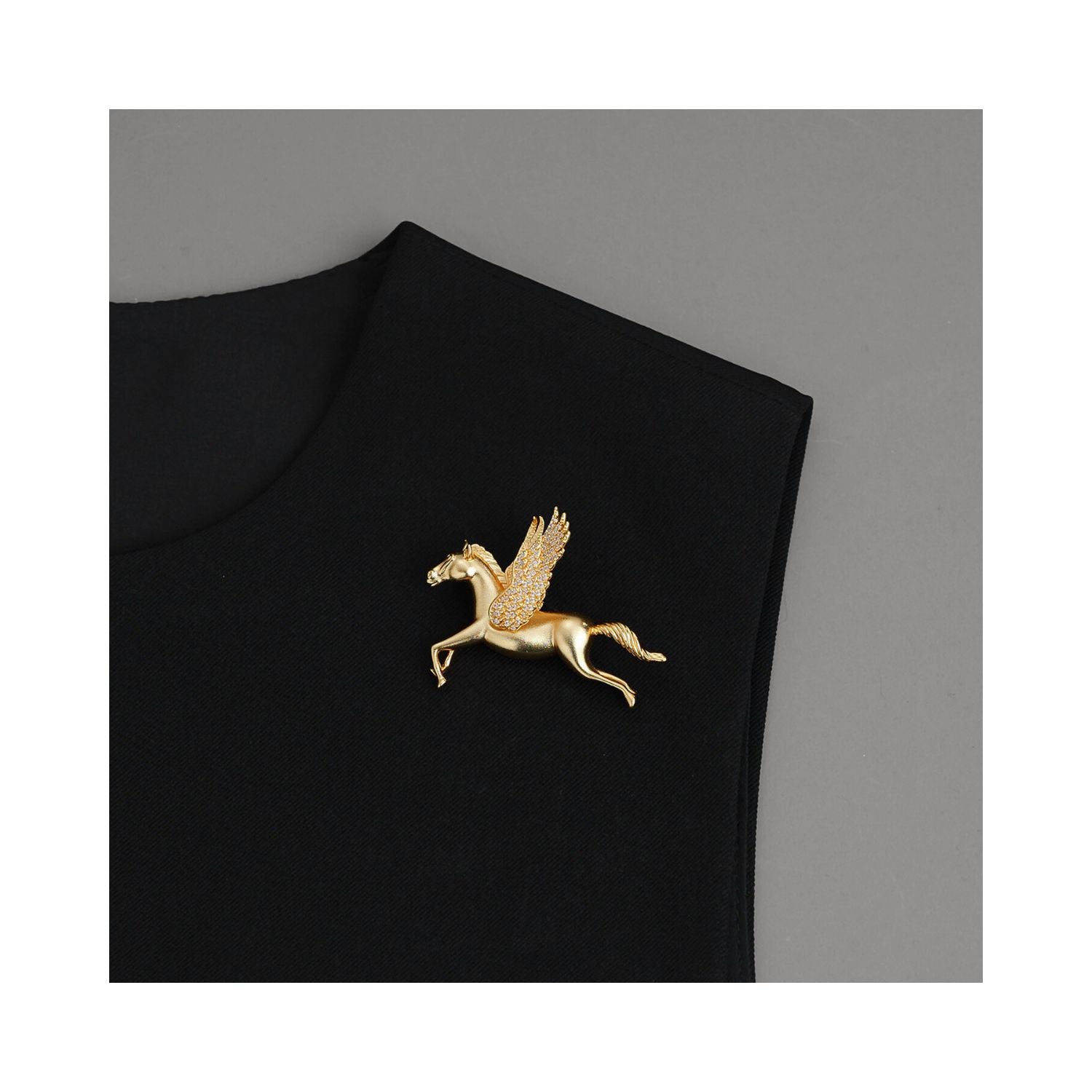 Gold-tone Wings of Inspiration Pegasus pavé horse brooch styled on a black lapel, showing an elegant flying horse silhouette and refined statement styling.