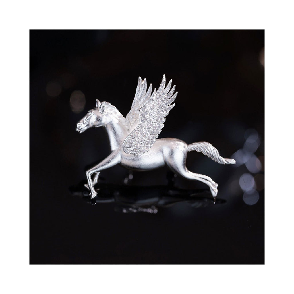 Close-up of Wings of Inspiration Pegasus pavé horse brooch in silver tone on a dark background, featuring the sculpted horse silhouette, pavé wing sparkle, and cool-toned shine.