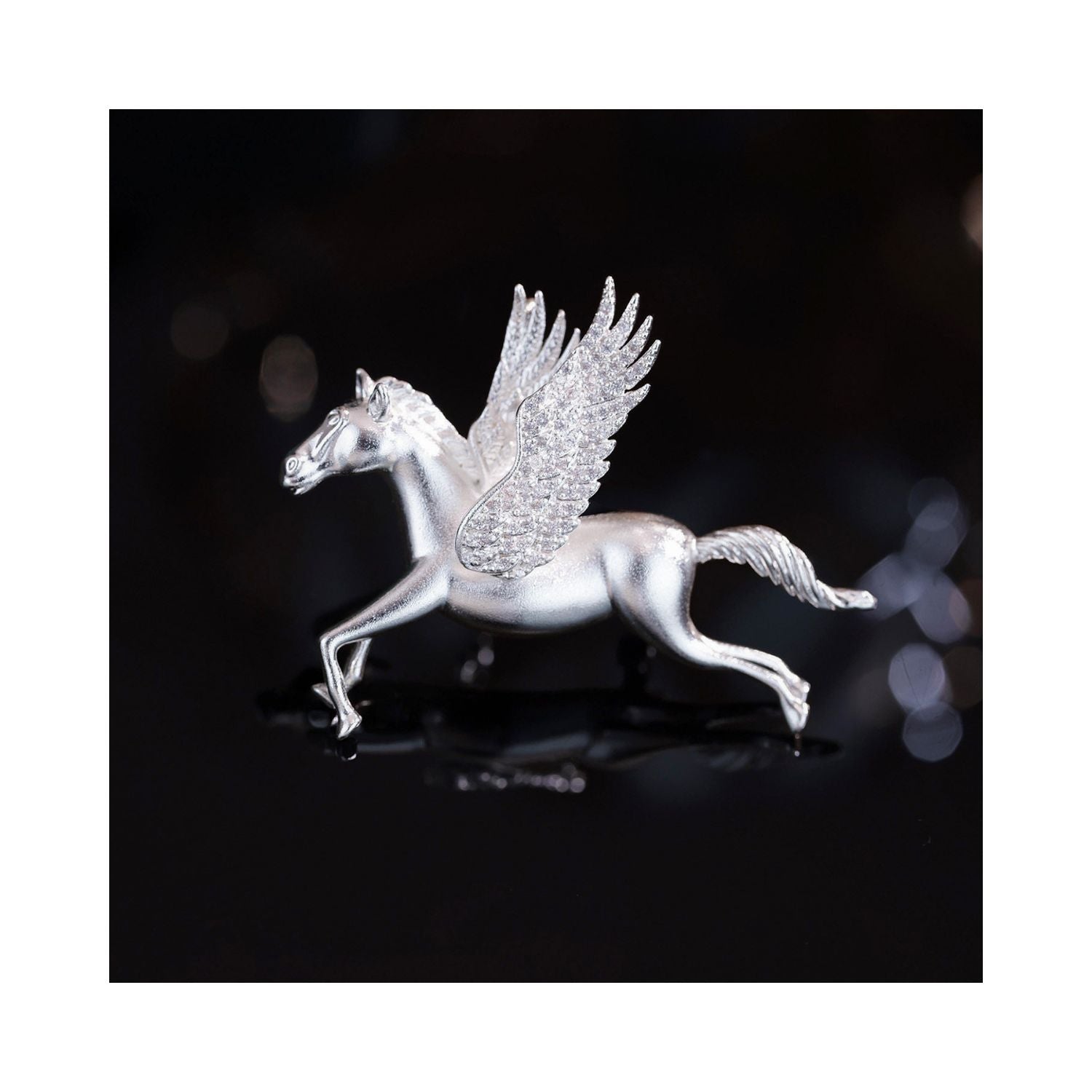 Close-up of Wings of Inspiration Pegasus pavé horse brooch in silver tone on a dark background, featuring the sculpted horse silhouette, pavé wing sparkle, and cool-toned shine.